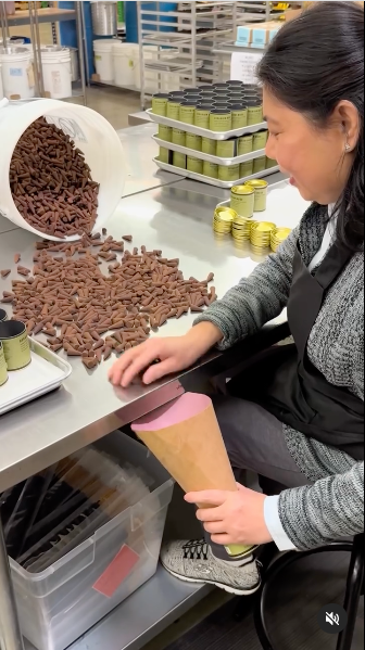 A woman operates machinery in a chocolate factory, focused on her task amidst a workspace filled with chocolate products